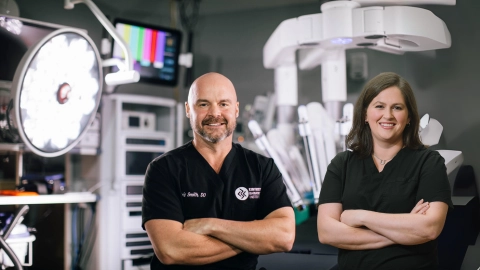 Dr. Eric Smith and Dr. Sarah Hayek in front of surgical robot